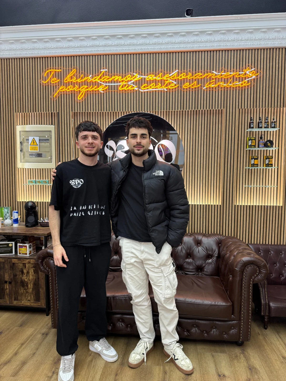 Interior de Barbería Pablo Olivares con dos personas frente al rótulo del local